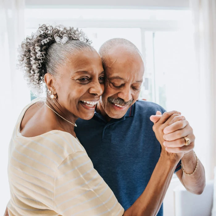 An older couple smiling warmly as they hold hands and dance together in a bright room